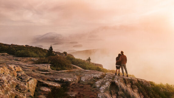 Mother and son stand at the summit of Cadillac Mountain at sunrise