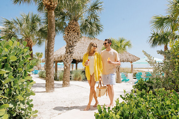 A couple walks infront of the Sandbar tiki bar at Treasure Island Beach Resort.